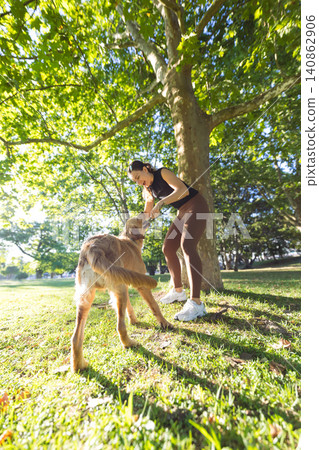Young woman in activewear plays with a golden retriever dog in a sunny park, surrounded by green trees and grass under a clear blue sky Young woman in activewear plays with a golden retriever dog in a sunny park, surrounded by green trees and grass under a clear blue sky 140862906