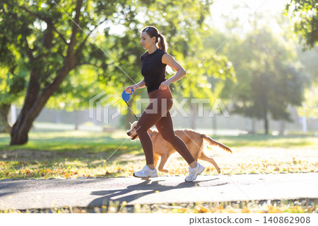 Woman jogging with a golden retriever dog on a sunny day in a park, surrounded by trees and green grass, wearing athletic clothing and sneakers Woman jogging with a golden retriever dog on a sunny day in a park, surrounded by trees and green grass, wearing athletic clothing and sneakers 140862908
