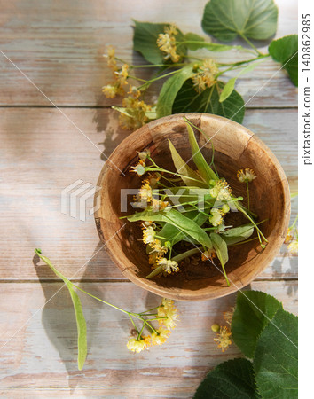 Linden flowers in wooden bowl on light wood 140862985