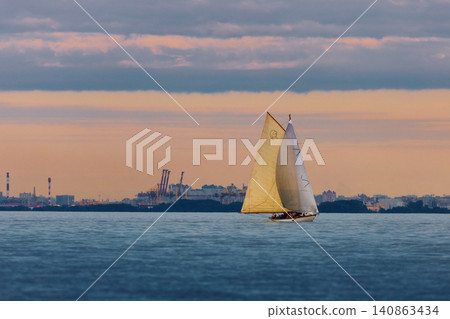 Vintage sailing boat through splashing water at sunset, Sailing regatta in the Gulf of Finland at sunset, hot race of several yachts, teamwork Vintage sailing boat through splashing water at sunset, Sailing regatta in the Gulf of Finland at sunset, hot race of several yachts, teamwork 140863434