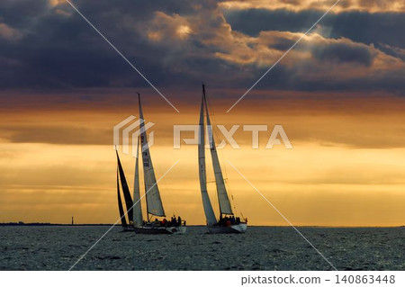 A lot of sailing boats are in sailing regatta in the Gulf of Finland at sunset, Russia, St.Petersburg, hot race of several yachts, teamwork, yachtsman 140863448