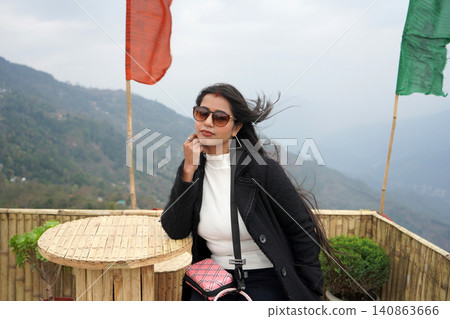 Stylish young woman sitting at a table with mountain view and prayer flags Stylish young woman sitting at a table with mountain view and prayer flags 140863666