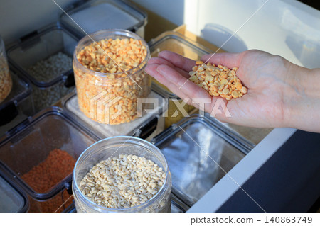 Woman's hand holds yellow split peas over an open kitchen drawer. Woman's hand holds yellow split peas over an open kitchen drawer. 140863749