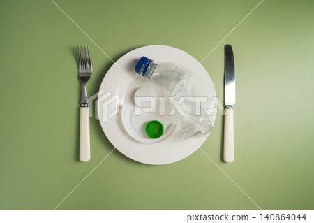 Plastic bottle served on plate with cutlery on green background, plastic pollution and waste concept 140864044