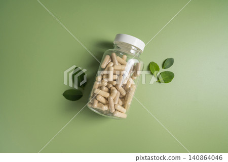 Herbal supplement capsules in bottle with leaves with green background, natural wellness concept 140864046