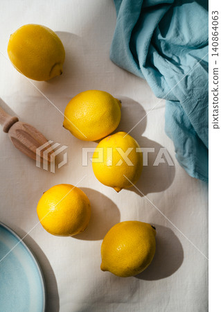 Whole lemons arranged on linen tablecloth with wooden citrus juicer in sunlight, minimalist food background Whole lemons arranged on linen tablecloth with wooden citrus juicer in sunlight, minimalist food background 140864063
