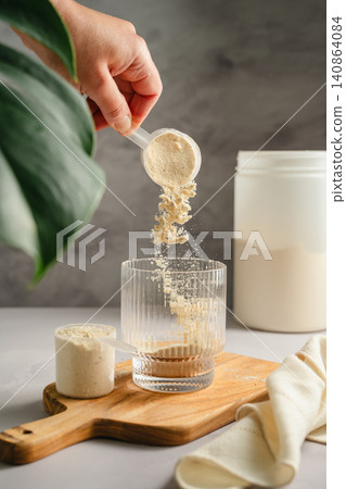 Adding whey protein powder to glass for shake preparation, sports nutrition supplement Adding whey protein powder to glass for shake preparation, sports nutrition supplement 140864084