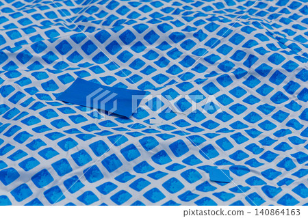 Repairing holes in an above ground pool liner with patches in the backyard Repairing holes in an above ground pool liner with patches in the backyard 140864163