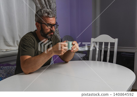 Adult man enjoys coffee while sitting at home workspace during morning break Adult man enjoys coffee while sitting at home workspace during morning break 140864592