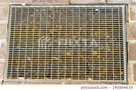 Top view of a rectangular metal drainage grate and scraper mat embedded in a brick pavement walkway. Top view of a rectangular metal drainage grate and scraper mat embedded in a brick pavement walkway. 140864639