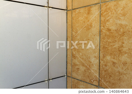 Close-up view of building facade installation showing contrasting white composite panels and orange marble texture porcelain tiles. Close-up view of building facade installation showing contrasting white composite panels and orange marble texture porcelain tiles. 140864643
