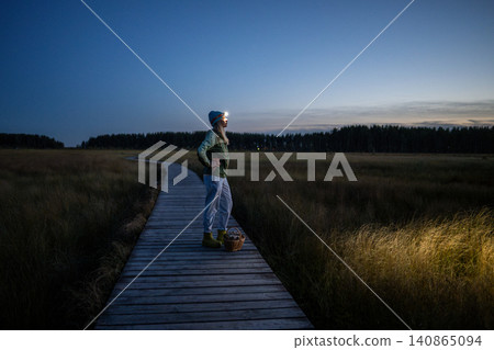 Woman forager taking moment to enjoy sunset on way home returning late from spending day in forest. Woman forager taking moment to enjoy sunset on way home returning late from spending day in forest. 140865094