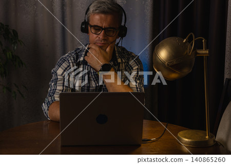 Freelancer working at night on laptop with headset in home office space Freelancer working at night on laptop with headset in home office space 140865260