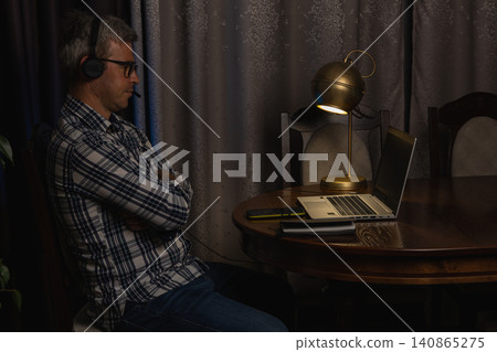 Man working from home at night on laptop with headset and notes 140865275