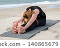 Woman practicing seated forward bend yoga pose on a sandy beach, promoting flexibility, mindfulness, relaxation, wellness, healthy lifestyle, and outdoor fitness 140865679