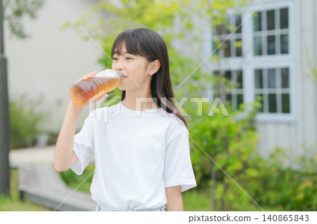 一個女孩用塑膠瓶喝大麥茶。 一個女孩用塑膠瓶喝大麥茶。 140865843