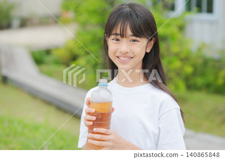 一個女孩拿著一瓶塑膠瓶裝的大麥茶 一個女孩拿著一瓶塑膠瓶裝的大麥茶 140865848