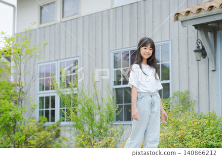 一個年輕女孩站在一棟獨立式住宅前。 140866212