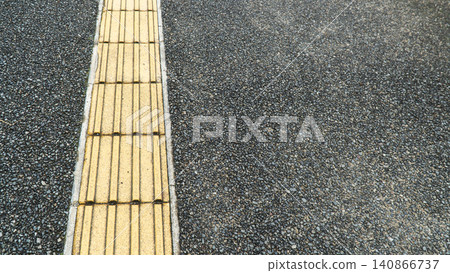 Yellow tactile paving blocks run diagonally across the dark asphalt sidewalk. Yellow tactile paving blocks run diagonally across the dark asphalt sidewalk. 140866737