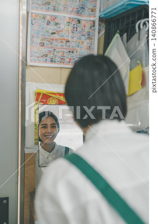 A female staff member checks her smile in the mirror in the back room of a supermarket. A female staff member checks her smile in the mirror in the back room of a supermarket. 140866771