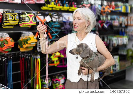 Elderly woman with dog choosing leash in pet store Elderly woman with dog choosing leash in pet store 140867202