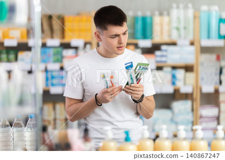 In sales area of pharmacy, guy examines packaging of toothbrush kit In sales area of pharmacy, guy examines packaging of toothbrush kit 140867247