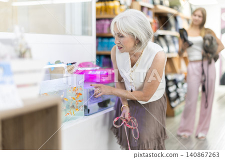 Elderly woman with dog watching aquarium fish in pet store Elderly woman with dog watching aquarium fish in pet store 140867263