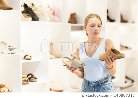 Young woman choosing clogs in clothing store Young woman choosing clogs in clothing store 140867315