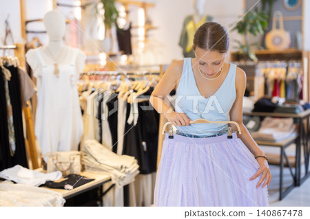 Young woman chooses skirt in clothing store Young woman chooses skirt in clothing store 140867478