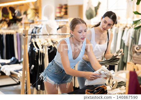 Two girls friends customer chooses denim knee breeches or shorts in store Two girls friends customer chooses denim knee breeches or shorts in store 140867590
