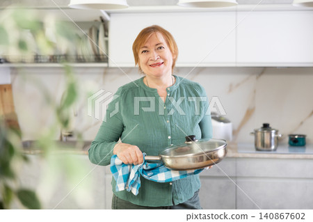 Happy mature woman cooking in her kitchen with radiant smile Happy mature woman cooking in her kitchen with radiant smile 140867602