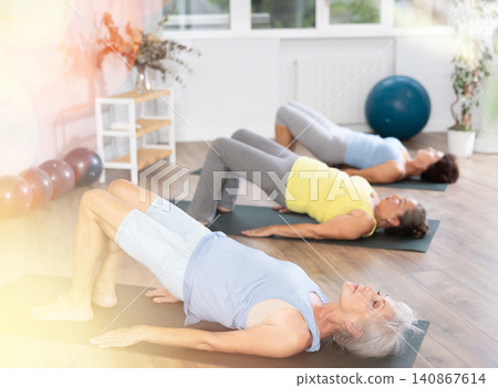 Old woman practicing bridge pose of yoga in training room during fitness classes Old woman practicing bridge pose of yoga in training room during fitness classes 140867614