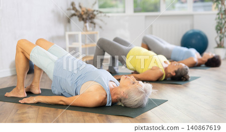 Old woman practicing bridge pose of yoga in training room during fitness classes Old woman practicing bridge pose of yoga in training room during fitness classes 140867619