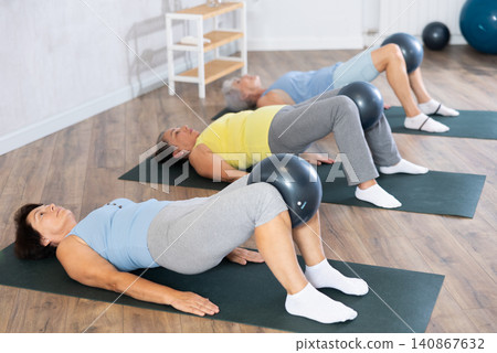 Elderly women perform softball exercises lying on floor, workout for beautiful figure, toned body Elderly women perform softball exercises lying on floor, workout for beautiful figure, toned body 140867632