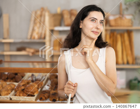 Young woman near window of bakery food court store examines assortment Young woman near window of bakery food court store examines assortment 140867647