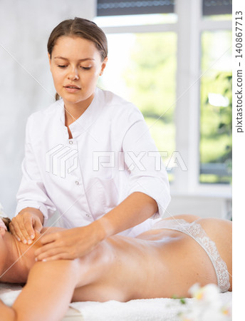 Young professional masseuse performing back massage to female client Young professional masseuse performing back massage to female client 140867713