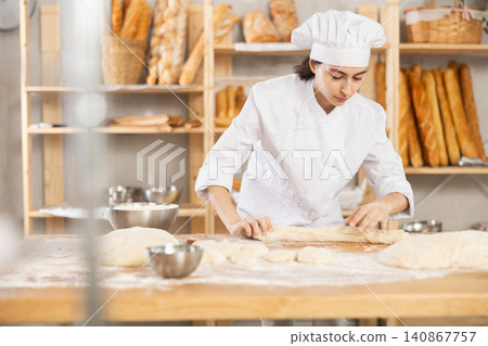 Young woman works as baker, mold baguette from dough, creates long loafs from dough. Young woman works as baker, mold baguette from dough, creates long loafs from dough. 140867757