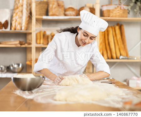 Young woman works in bakery as baker, kneads dough, works with flour. 140867770