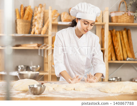 Young female baker kneading dough on table Young female baker kneading dough on table 140867788