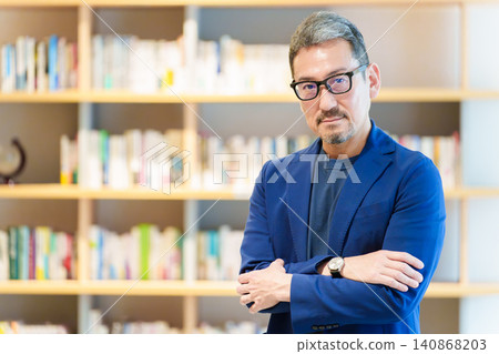 A middle-aged man standing in front of a bookshelf; author, writer, essayist. A middle-aged man standing in front of a bookshelf; author, writer, essayist. 140868203