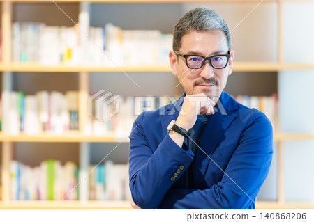 A middle-aged man standing in front of a bookshelf; author, writer, essayist. A middle-aged man standing in front of a bookshelf; author, writer, essayist. 140868206