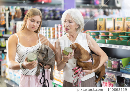 Girl and elderly woman choosing dog food together with dachshund in pet store Girl and elderly woman choosing dog food together with dachshund in pet store 140868539