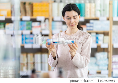 Girl in autumn clothes buys medicinal ointment or gel at pharmacy 140868665