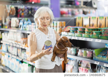 Senior woman chooses dog food for dachshund in pet store. Senior woman chooses dog food for dachshund in pet store. 140868675