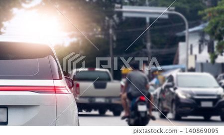 Bright lens flare illuminates a busy city street where a white car stands in traffic during peak hours. Motorcycle rider moves ahead alongside other vehicles. Car stop and turn on brake light. 140869095