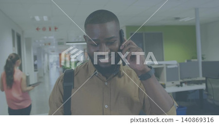 Walking man in brown button-up shirt talking on smartphone, with backpack strap in office corridor Walking man in brown button-up shirt talking on smartphone, with backpack strap in office corridor 140869316
