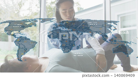 Kneeling therapist guiding patient on exercise mat in home clinic, wearing medical top, digital map Kneeling therapist guiding patient on exercise mat in home clinic, wearing medical top, digital map 140869409