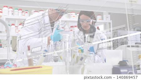 Pipetting two scientists wearing labcoats goggles and nitrile gloves at busy lab bench with pipette Pipetting two scientists wearing labcoats goggles and nitrile gloves at busy lab bench with pipette 140869457