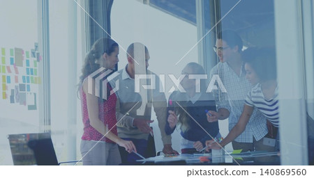 Leaning over conference table, five colleagues pointing at papers in glass room with sticky notes Leaning over conference table, five colleagues pointing at papers in glass room with sticky notes 140869560