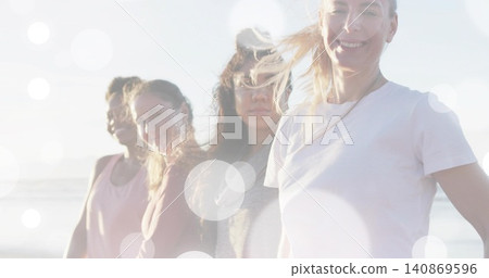 Standing four women smiling, wind-tossing hair on sunlit shore, ocean flare showing tees and studs Standing four women smiling, wind-tossing hair on sunlit shore, ocean flare showing tees and studs 140869596